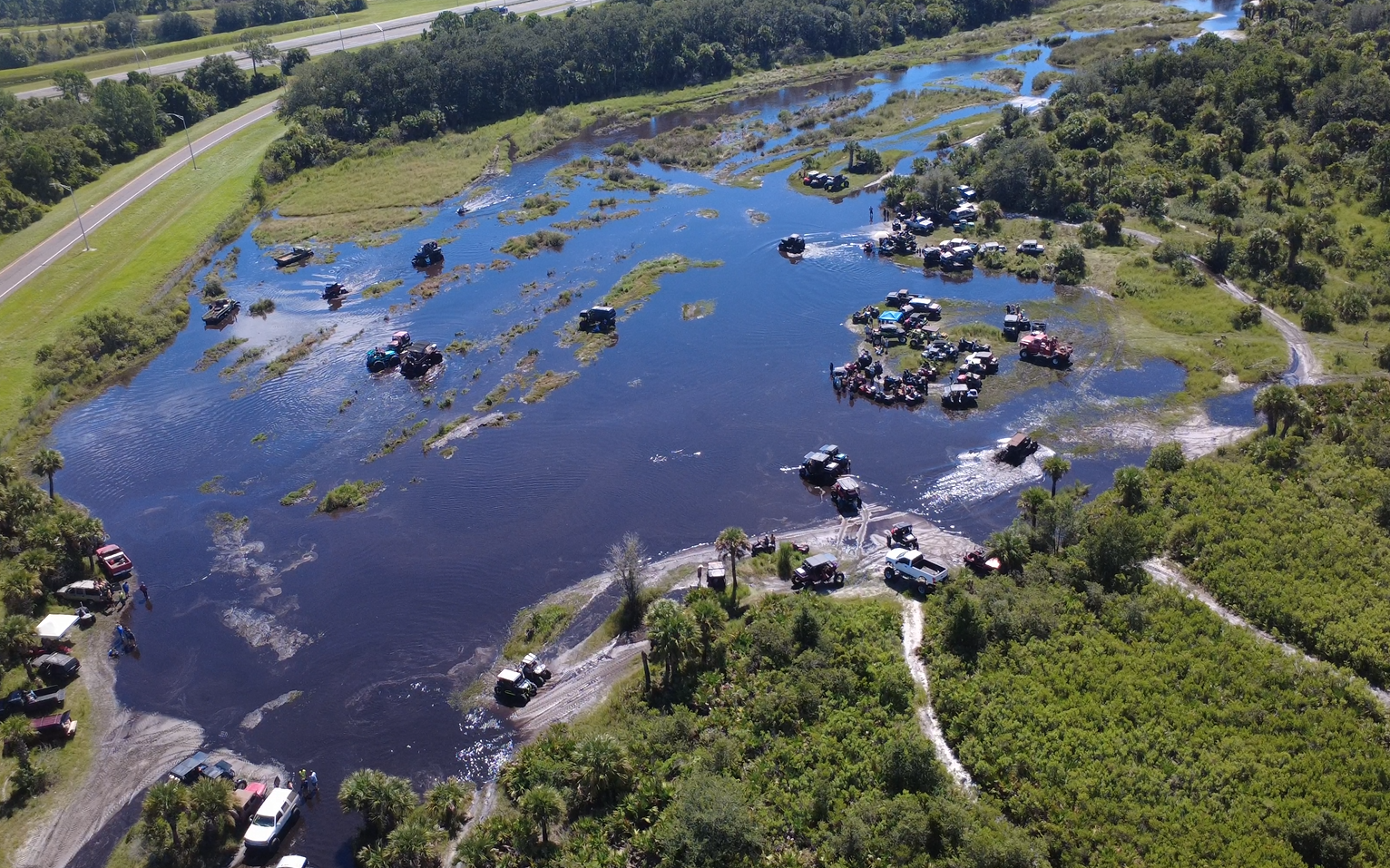 Wide aerial view of an off-road gathering around a flooded trail area